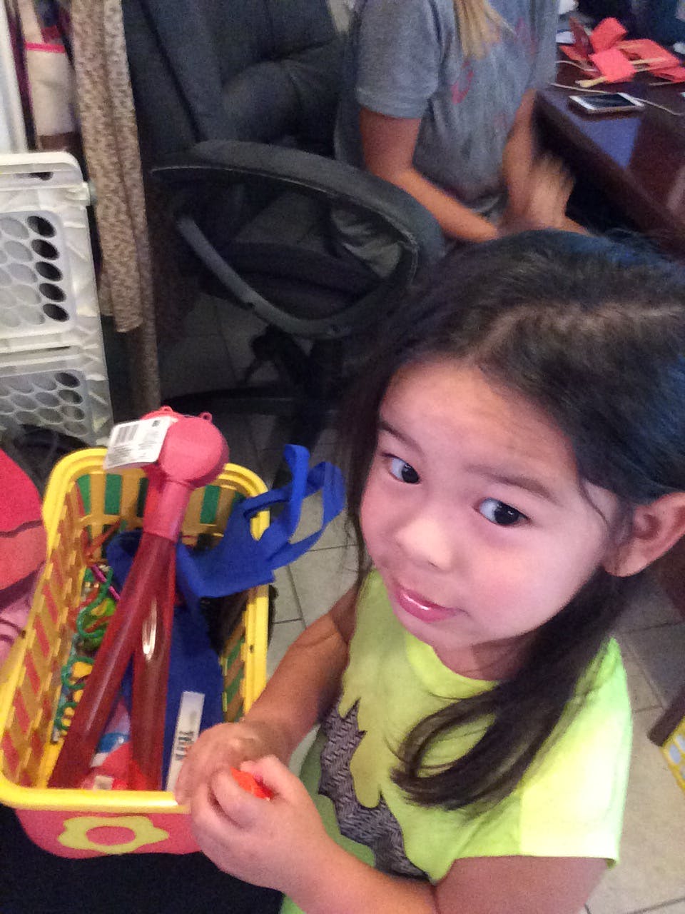 Child holding a small orange object next to a toy basket