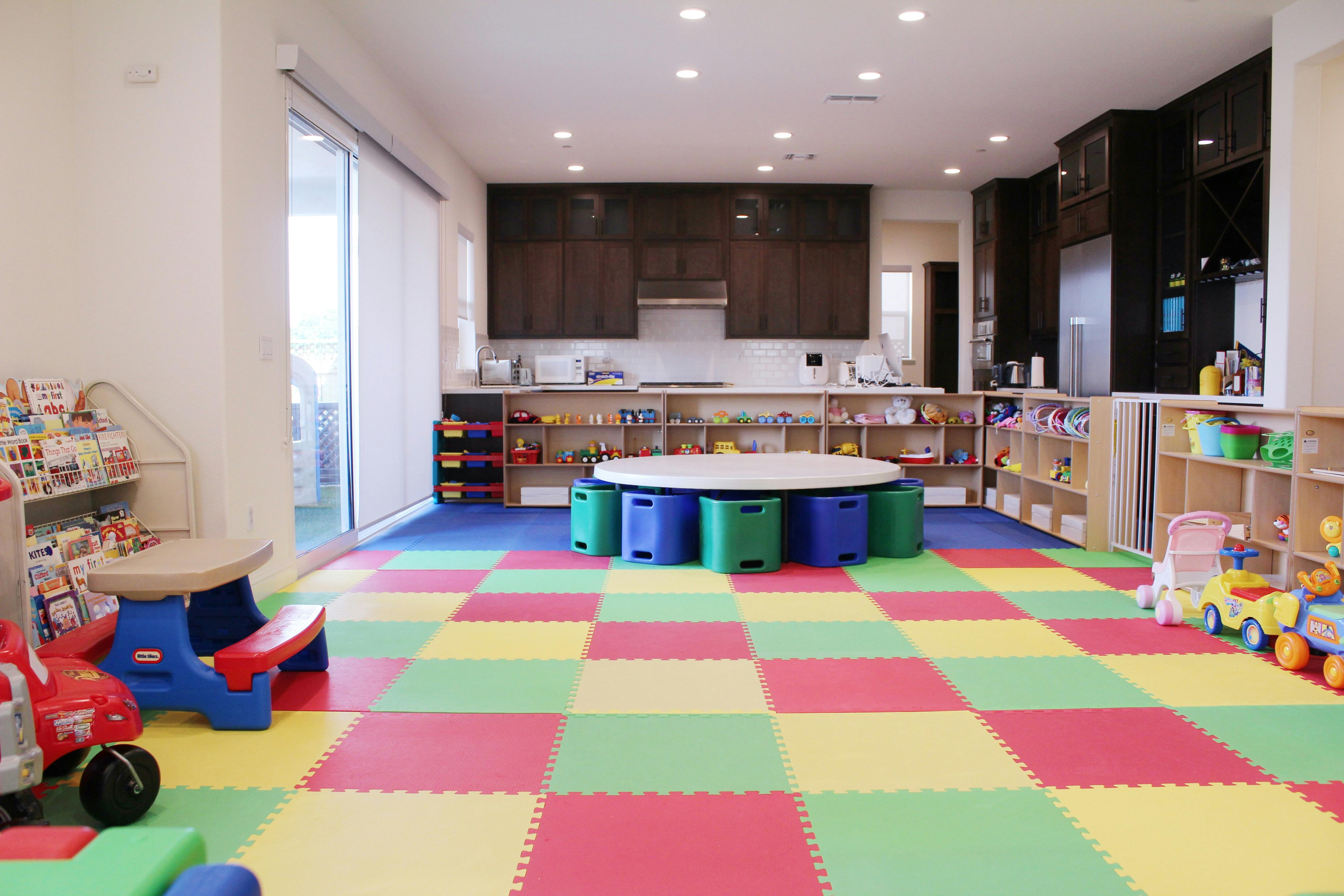 Playroom with colorful floor mats, toys, and a round table with storage bins