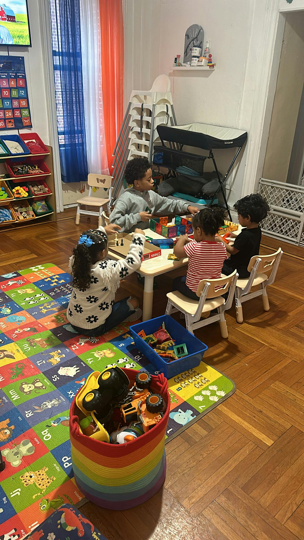 Four children playing with toys at a small table and on a colorful mat