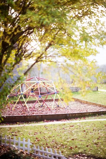 A geodesic dome climber on a playground with wood chips and fallen leaves