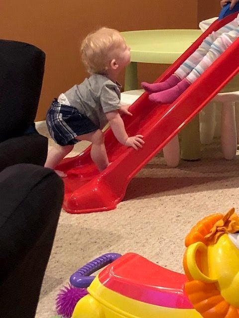 Child climbing up a red slide indoors
