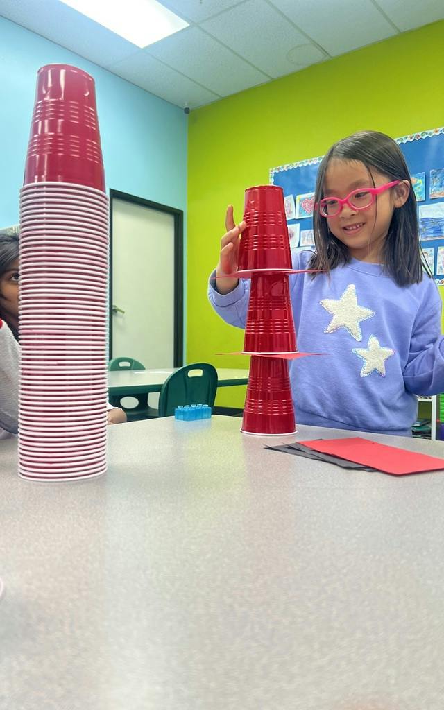 Child stacking red plastic cups and paper squares on a table