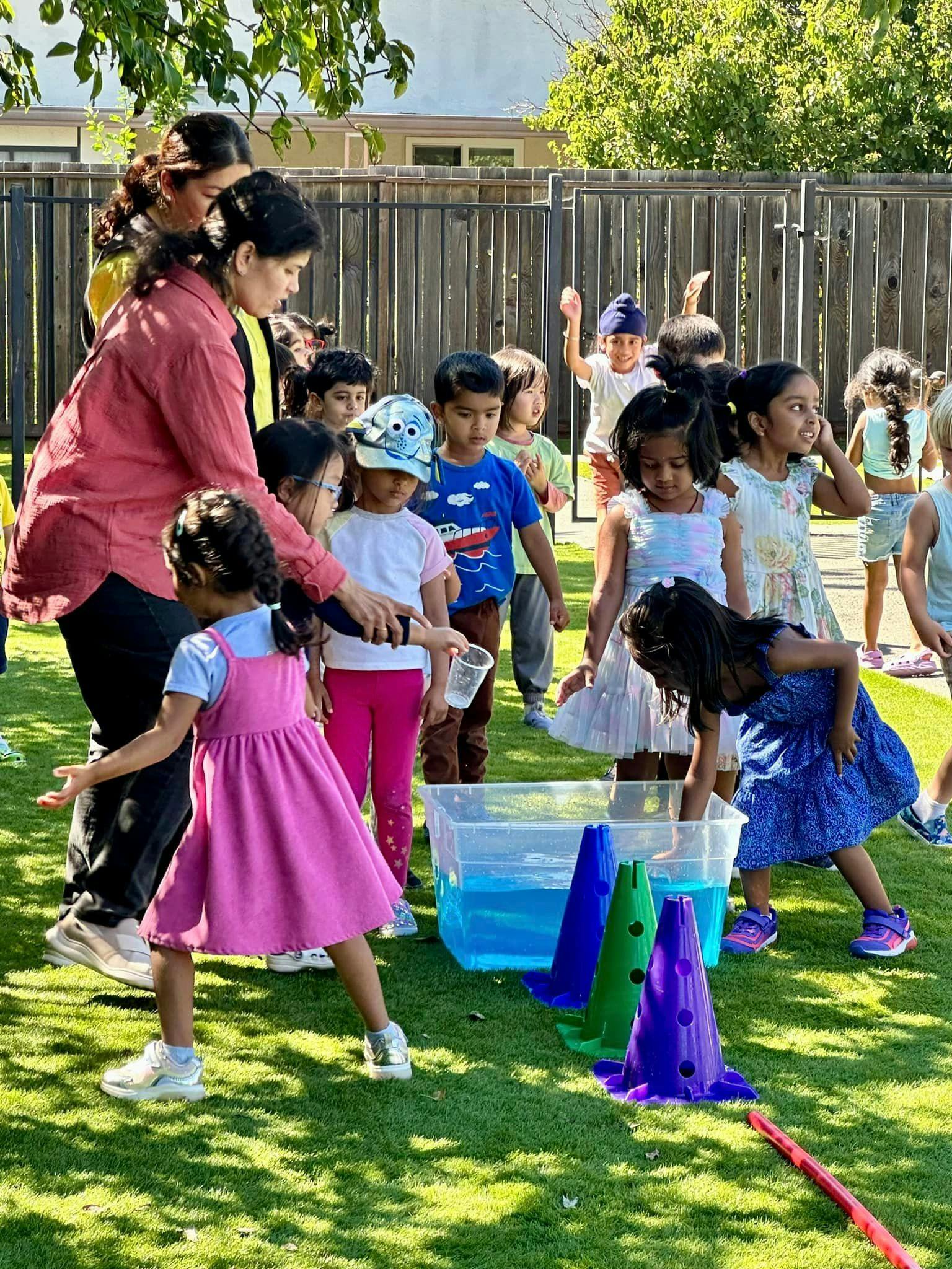 Adult and children playing with water in a plastic bin outdoors