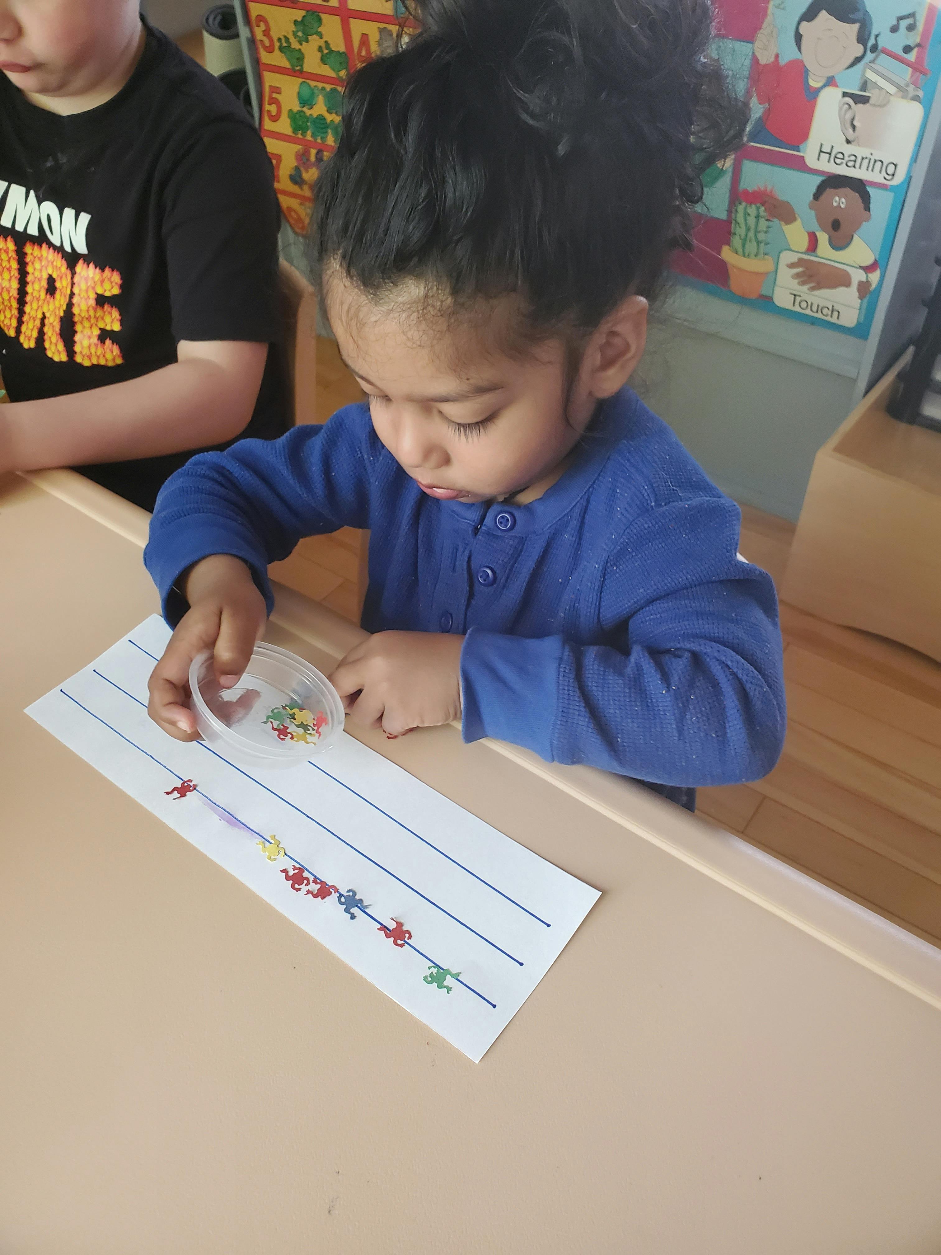 Child sorting small colorful objects onto a lined paper
