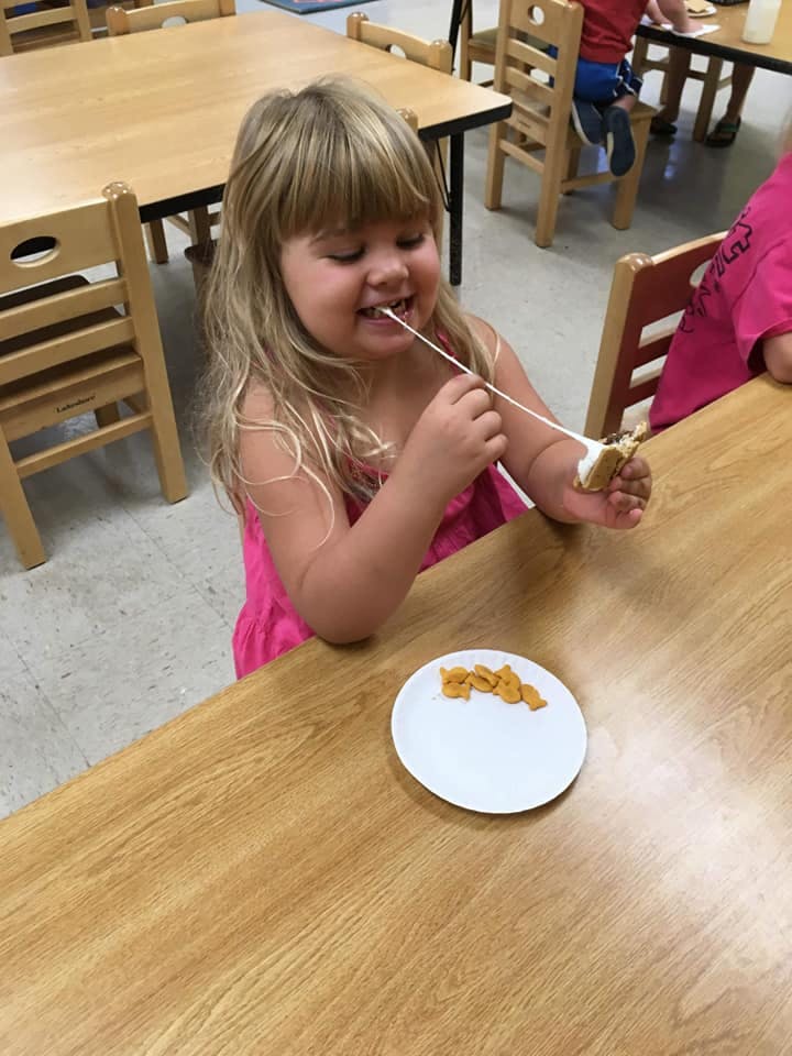 Child eating a snack with a stick at a table