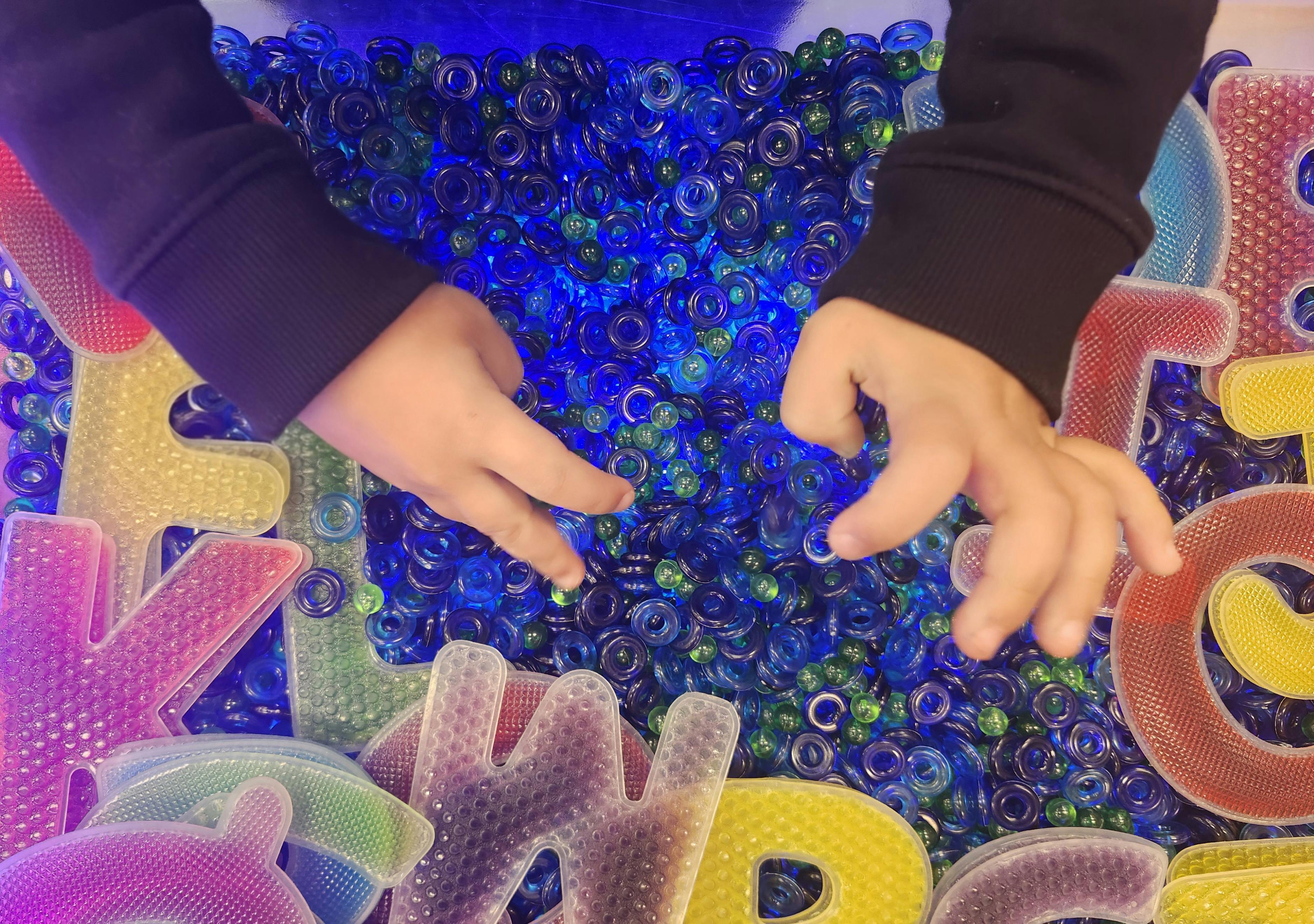 Child's hands playing with blue beads and colorful letter shapes