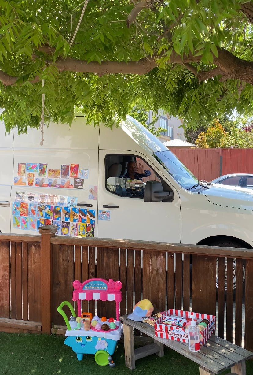 Ice cream truck with menu items on the side, toy cart and bench in foreground
