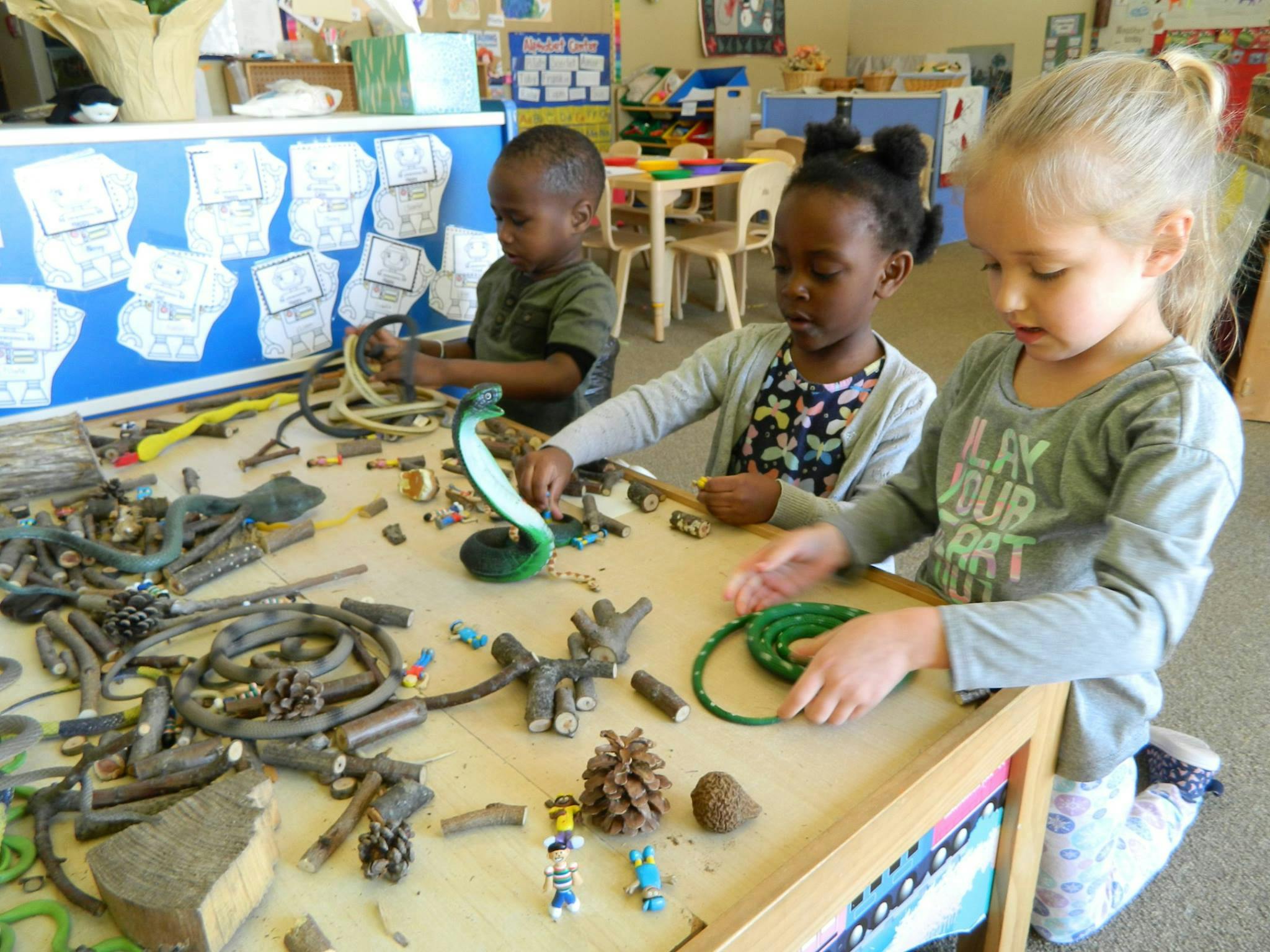 Three children playing with natural materials and crafts at a table