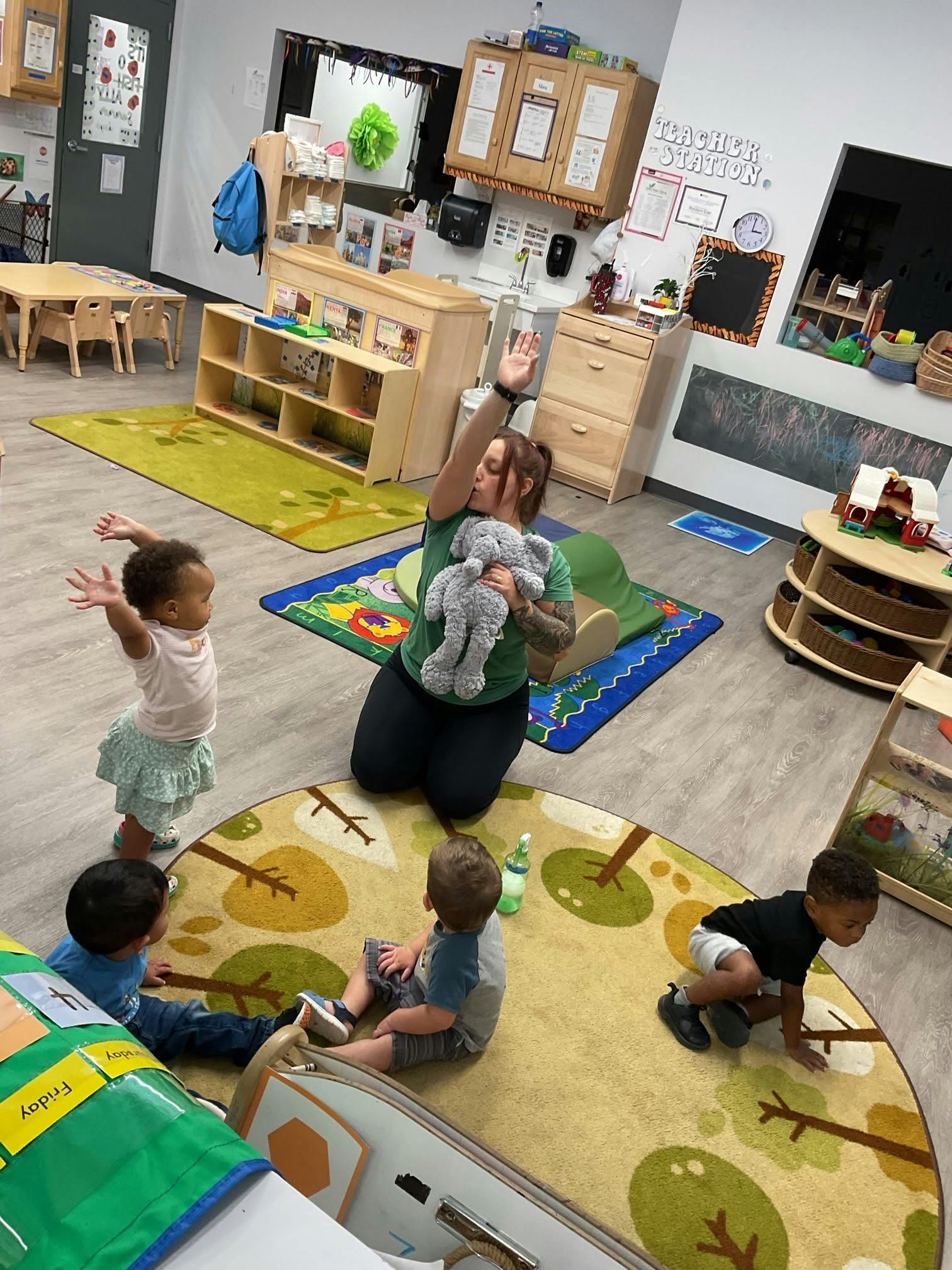 Teacher holding a stuffed animal and children sitting on the floor in a classroom