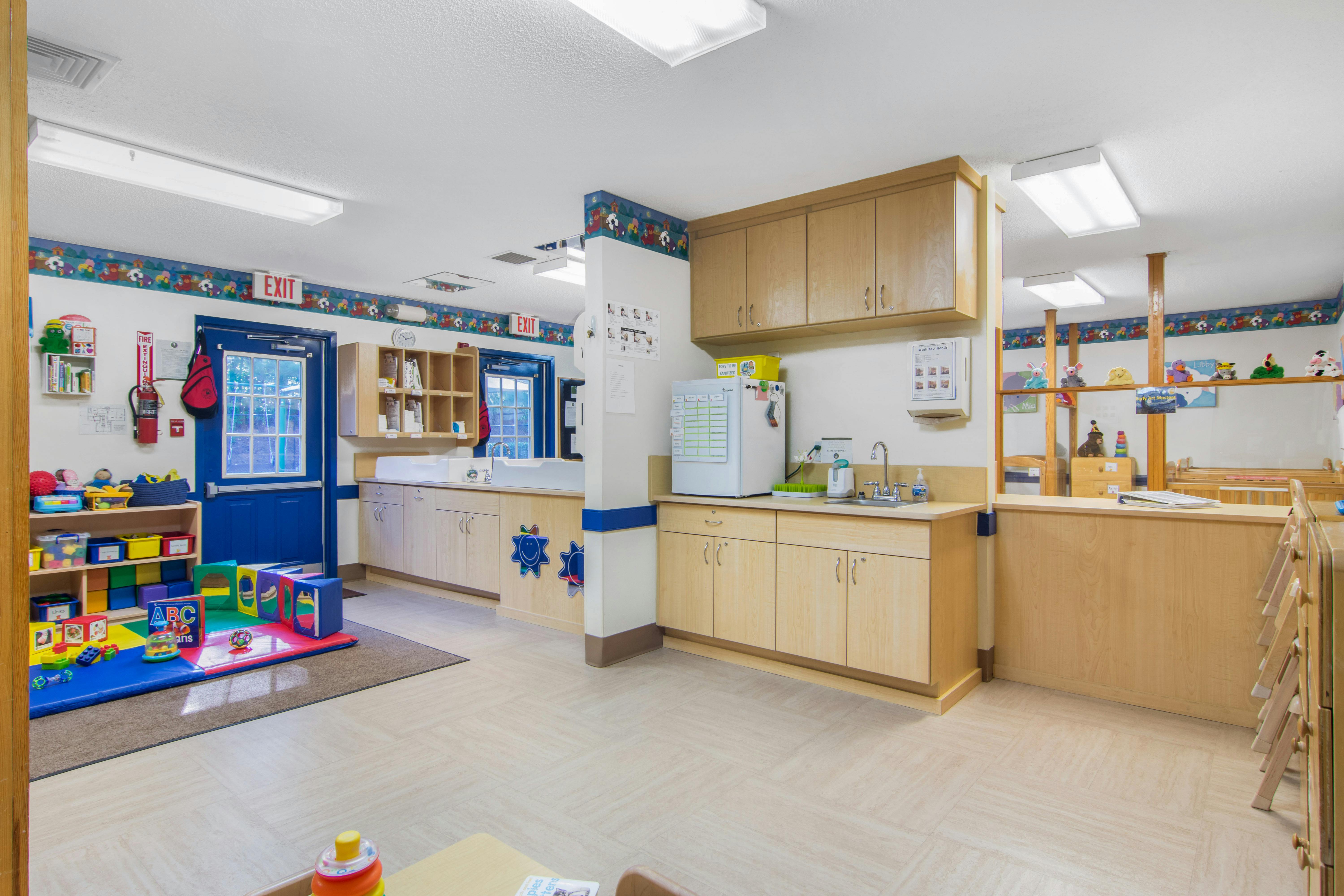 Classroom interior with play mat, storage shelves, sinks, and exit doors