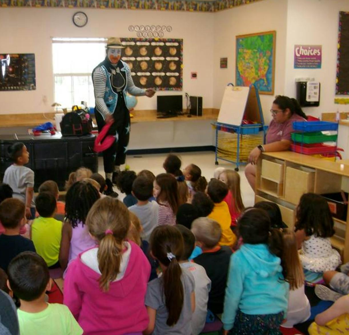 Person in clown makeup performing for children in a classroom