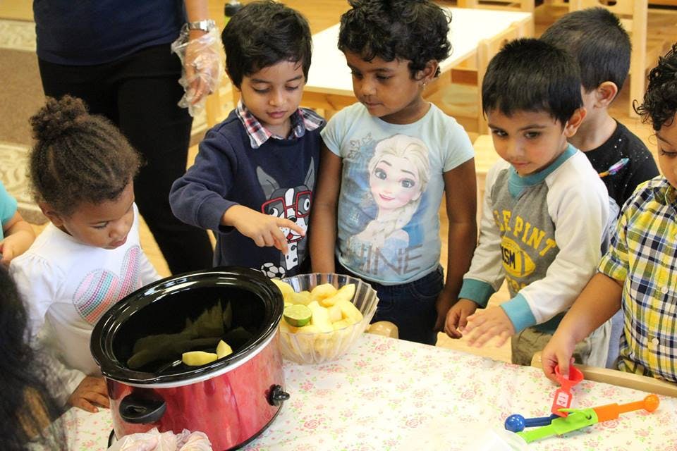Children gathered around a slow cooker and bowl of fruit