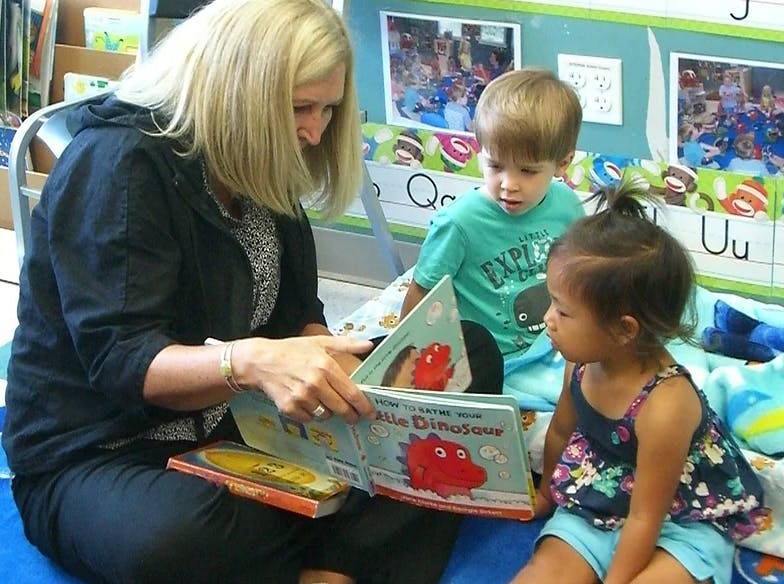 Person reading a book to two children in a classroom