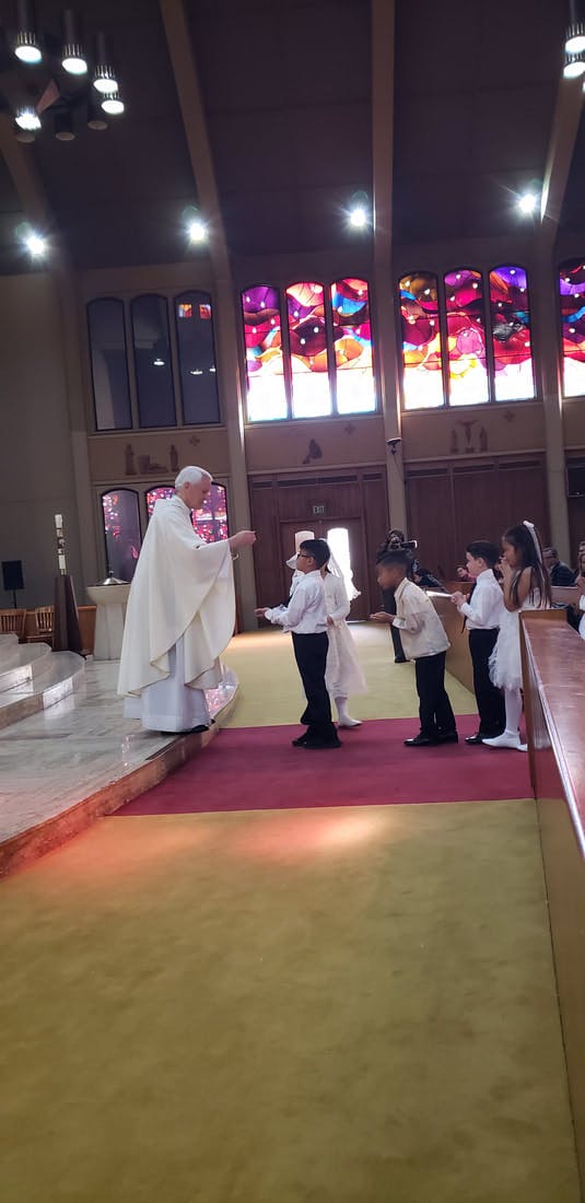 A person in a white robe offering communion to children in a church