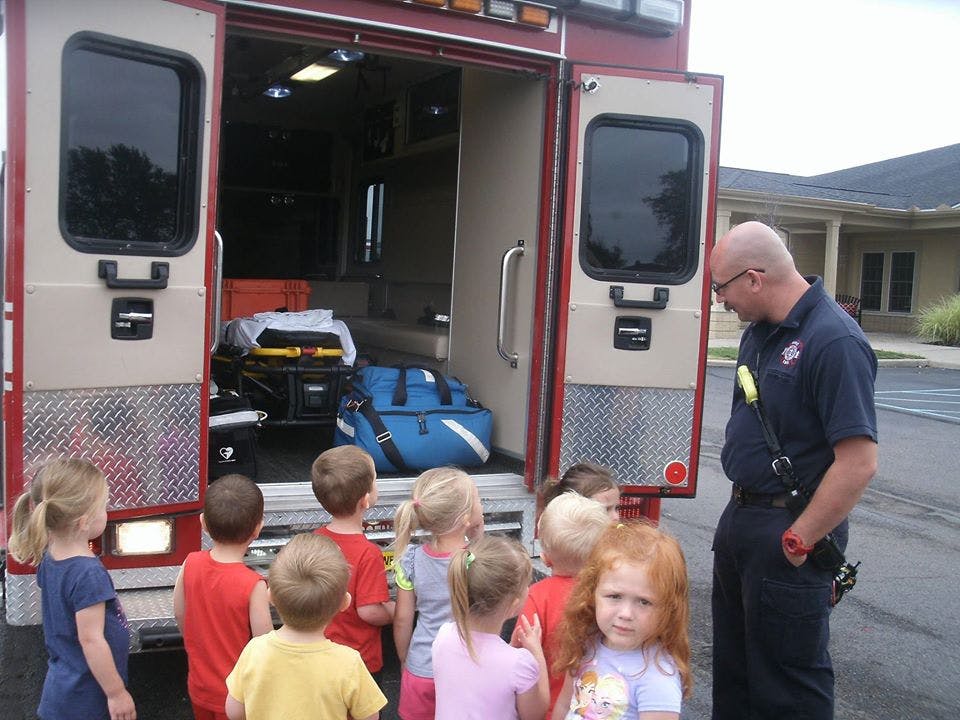 Person in uniform with children looking at the back of an ambulance