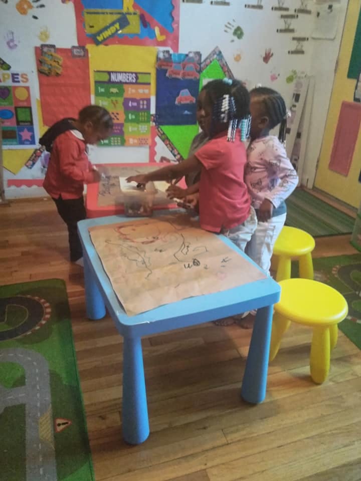 Three children drawing at a table in a classroom