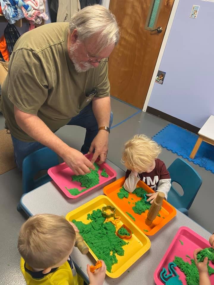 Adult and children playing with green kinetic sand at a table