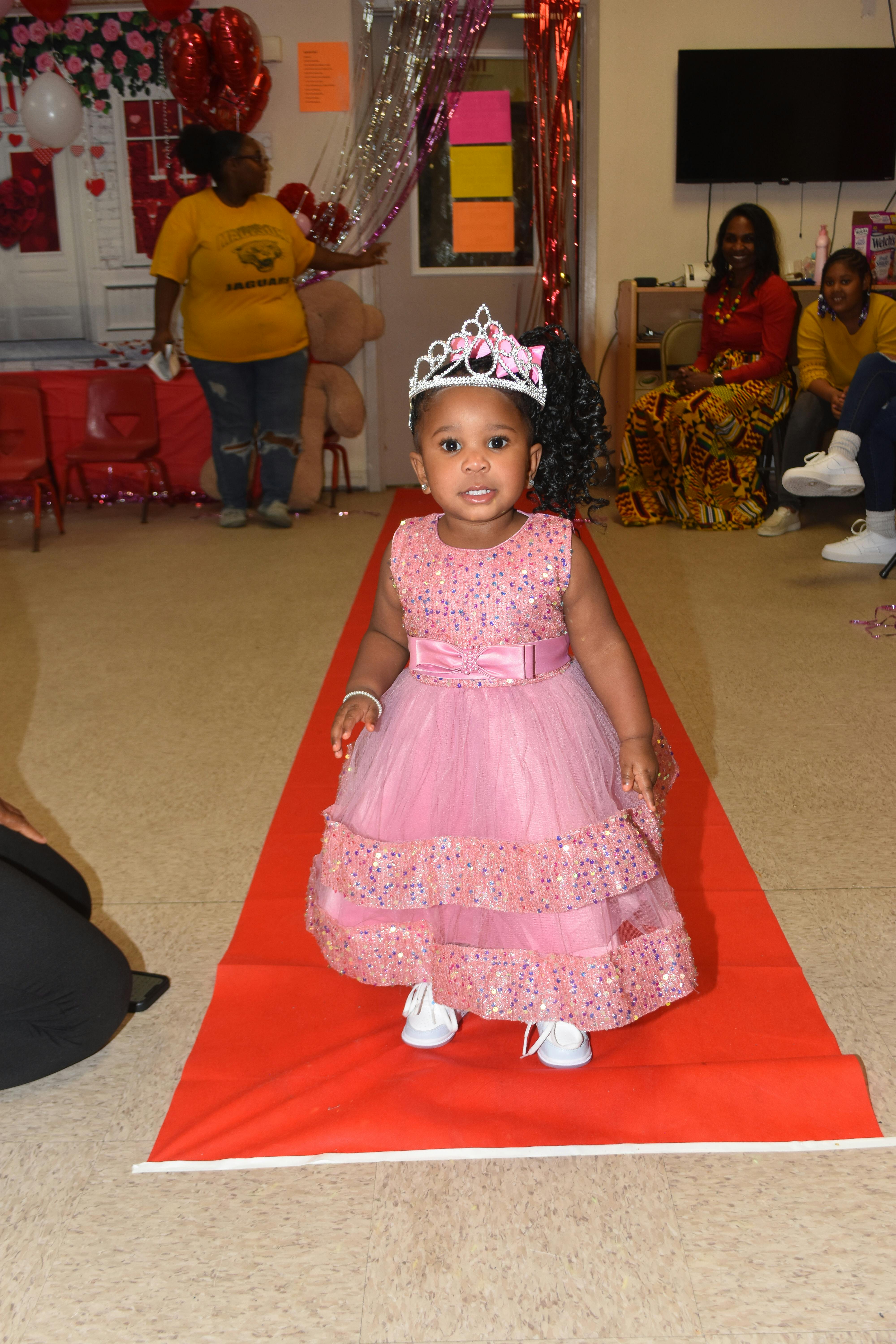 Child wearing a pink dress and tiara on a red carpet