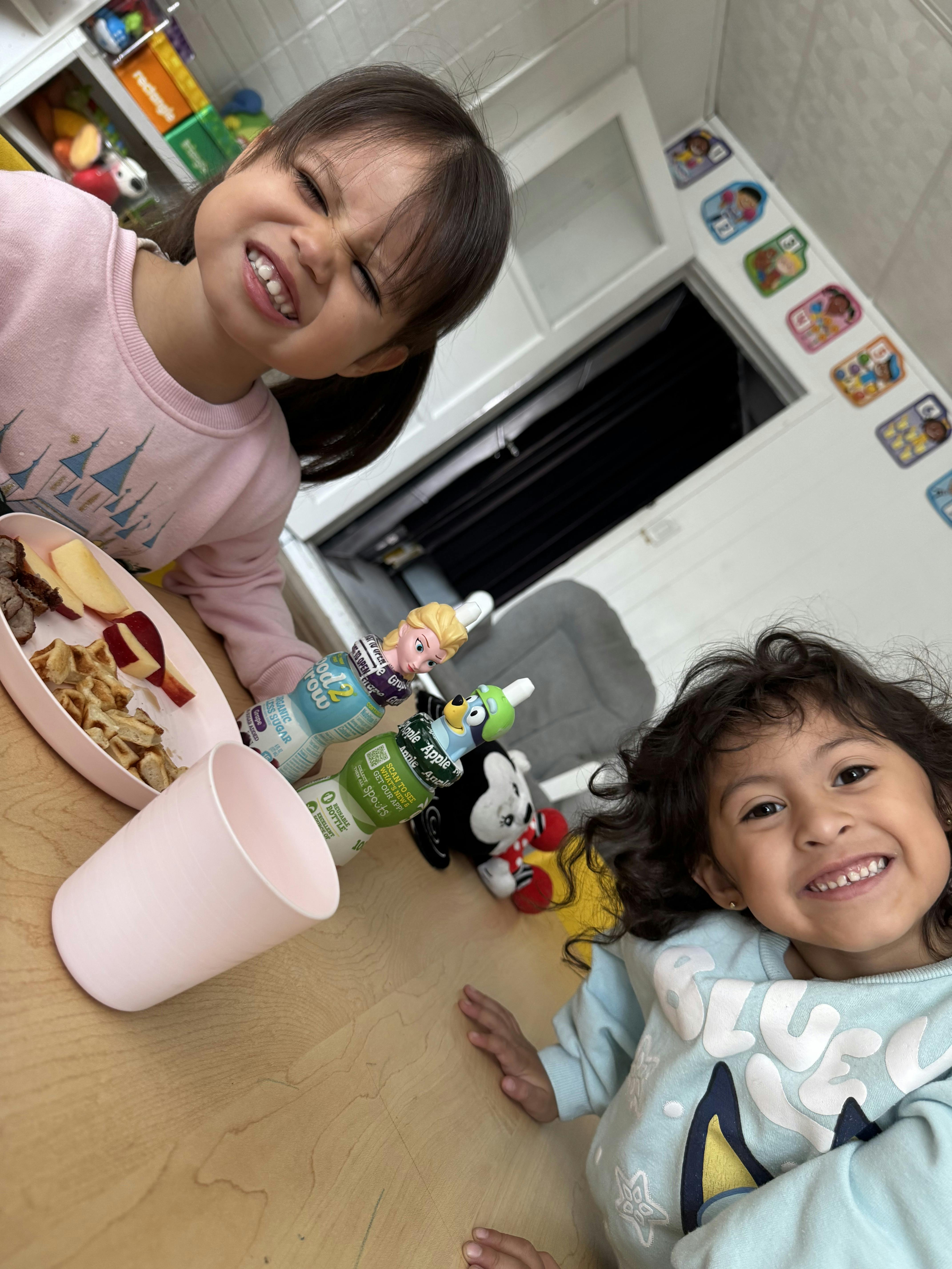 Two children at a table with a plate of food and drinks