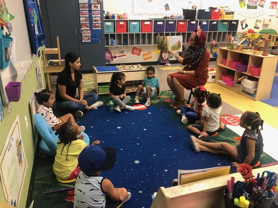 Adults reading to children sitting on a rug in a classroom