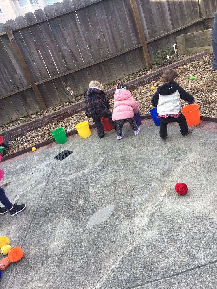 Three children playing with buckets and balls outdoors
