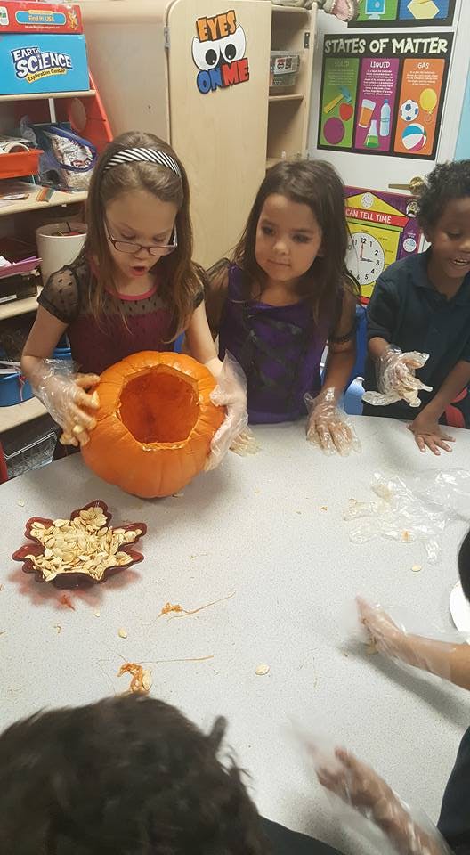 Children wearing gloves carving a pumpkin in a classroom