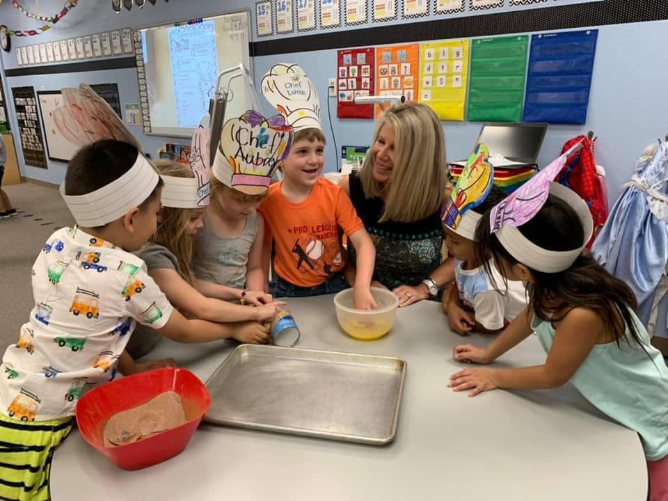 Adult and children in chef hats mixing ingredients in a classroom
