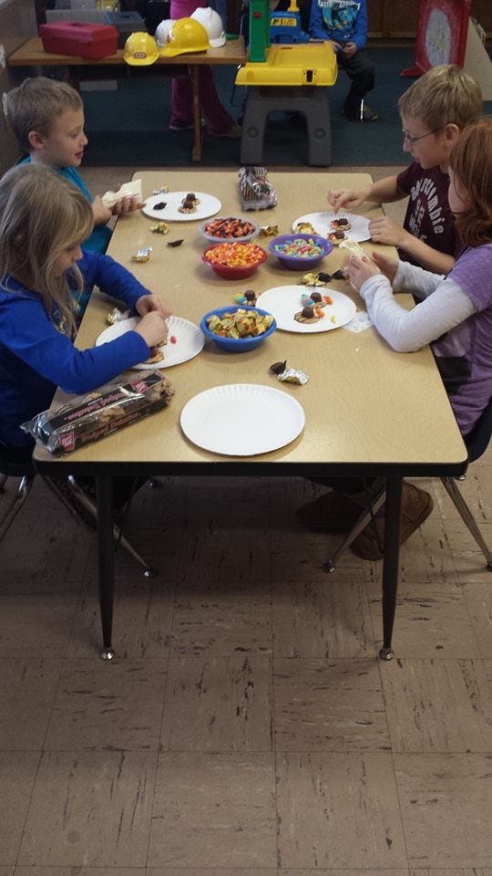 Four children sitting at a table making crafts with candy and snacks