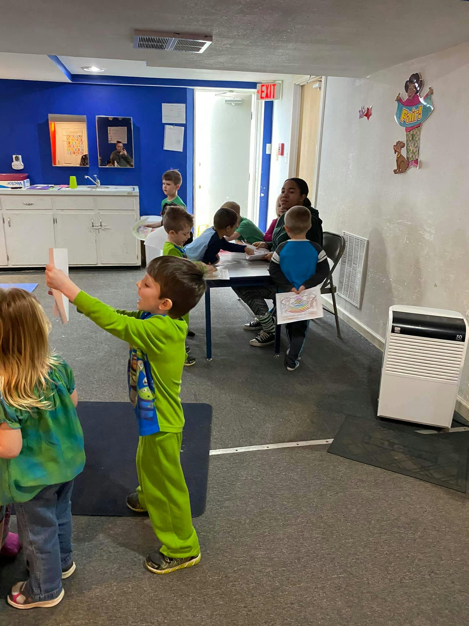 Children in a classroom, one child holding up a paper