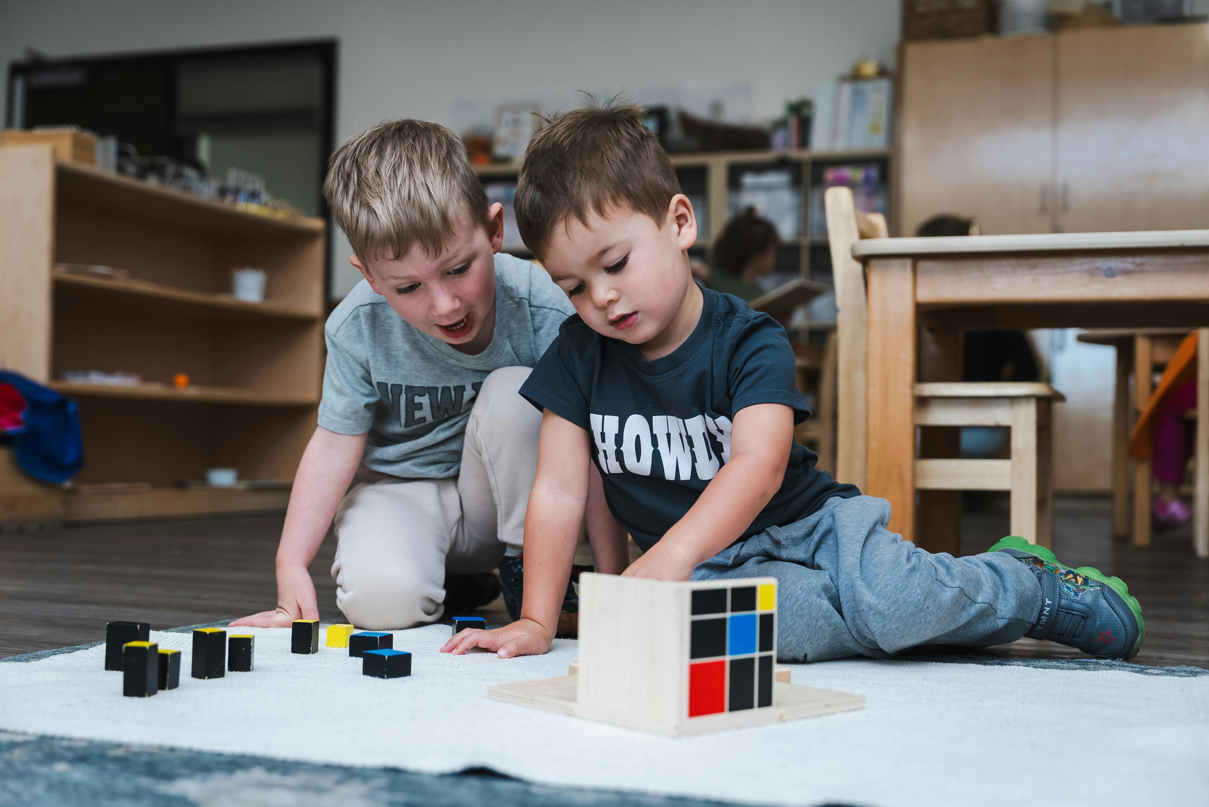 Two children playing with blocks on the floor in a classroom