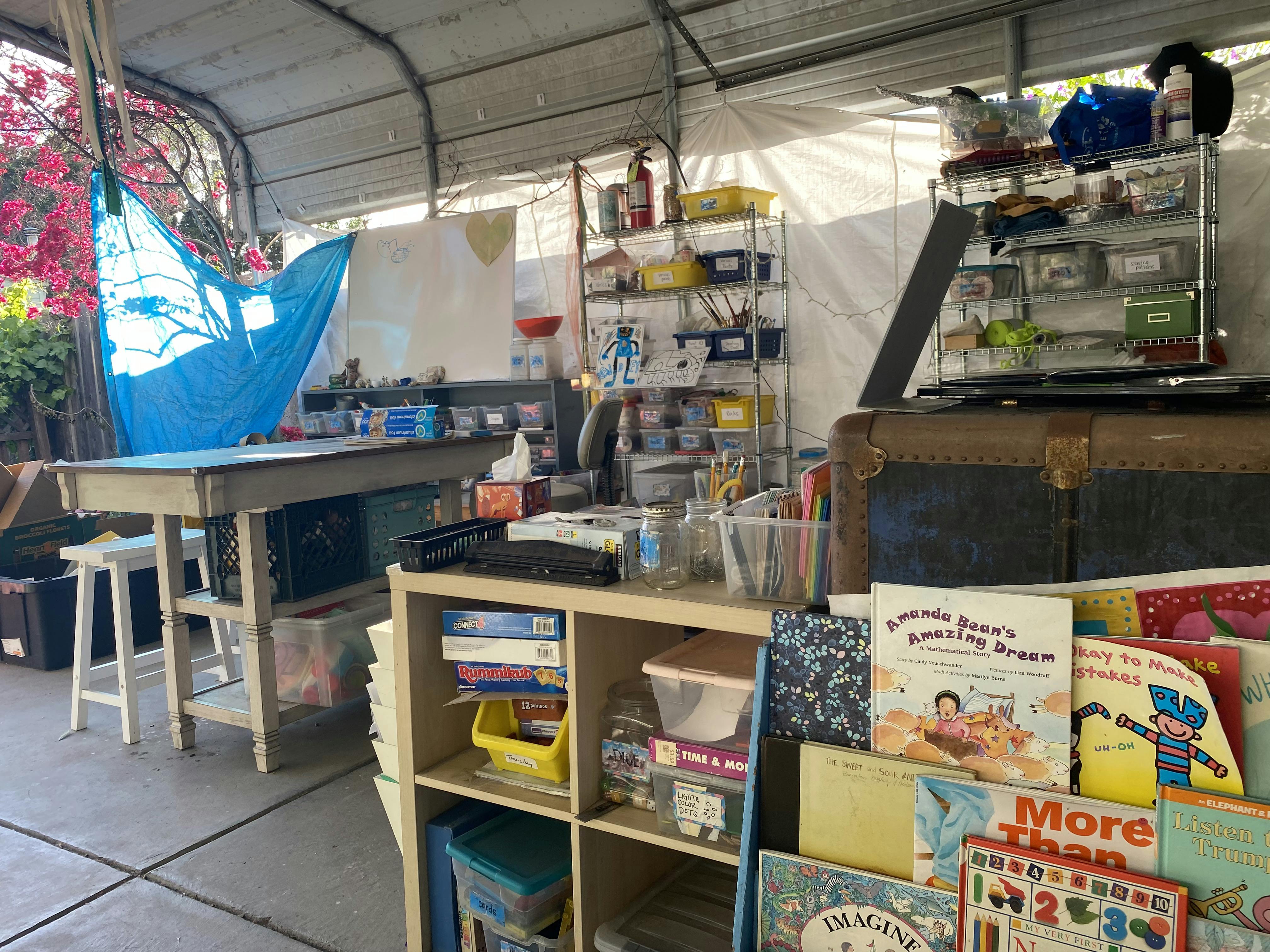An outdoor art studio with a white board, craft supplies, books, and work tables