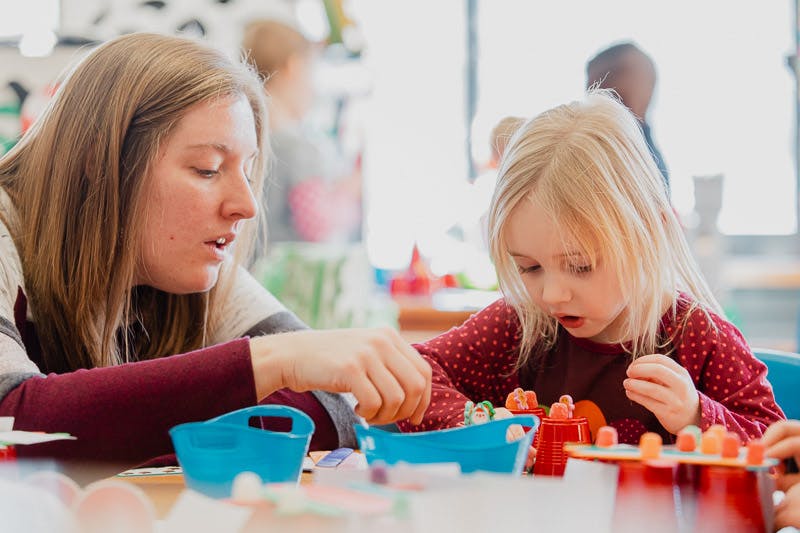 Person and child playing with small objects at a table