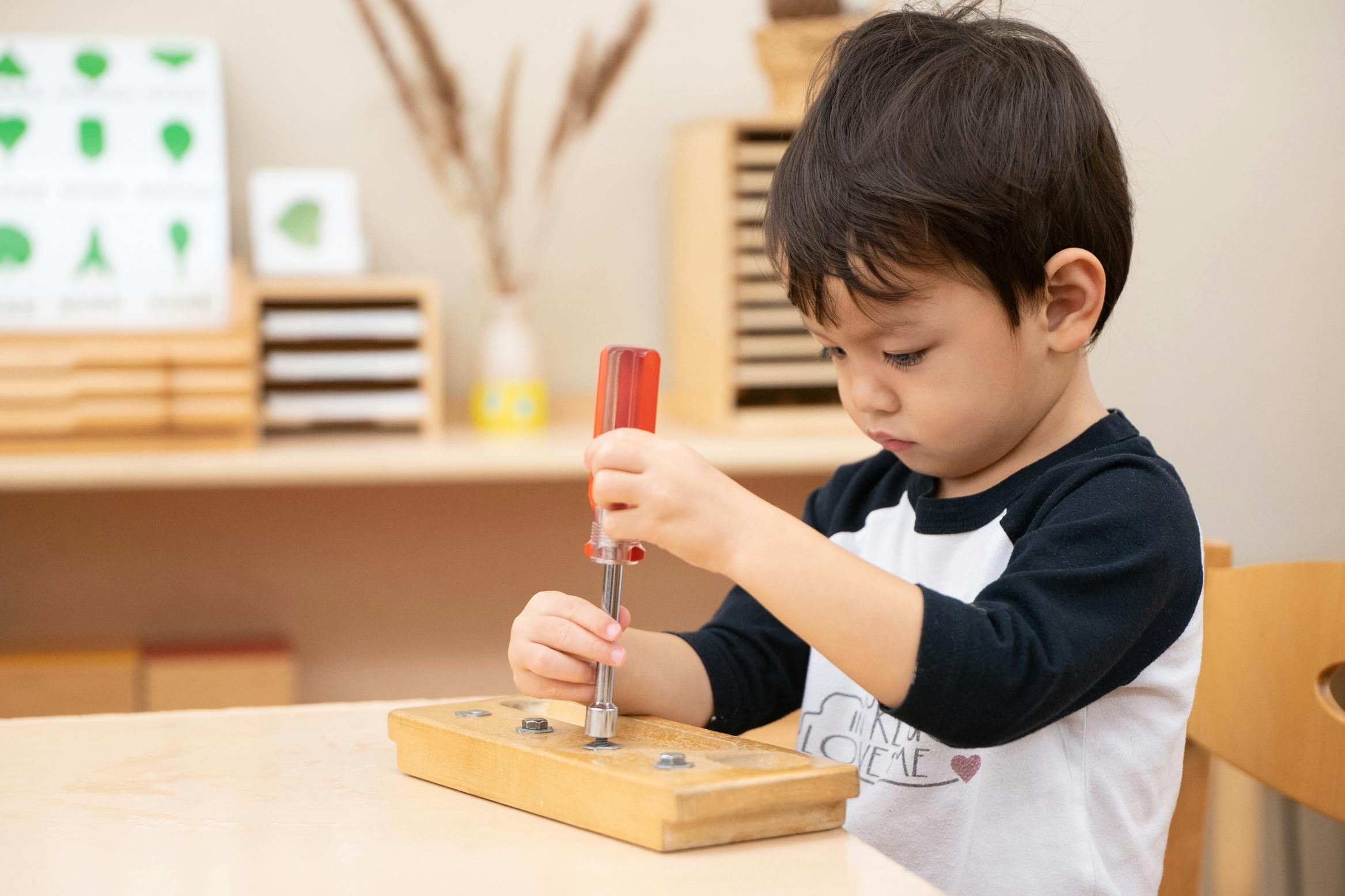 Child using a screwdriver on a wooden block with screws