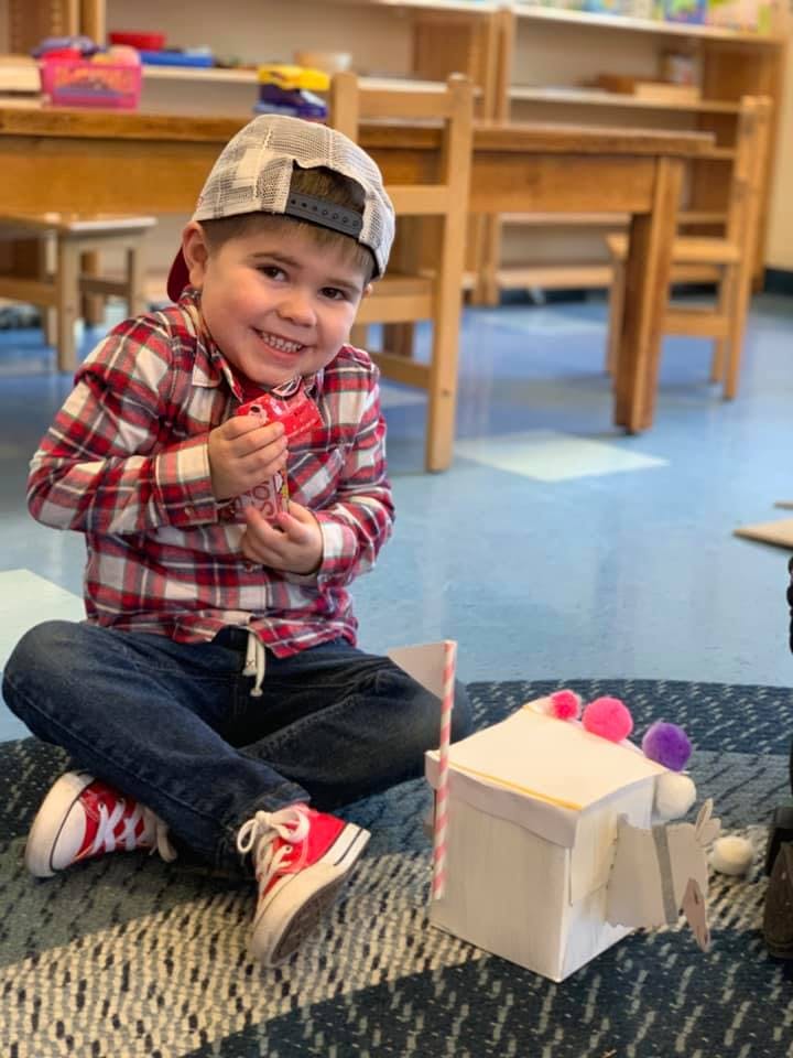Child in a plaid shirt and hat sitting on the floor holding a toy