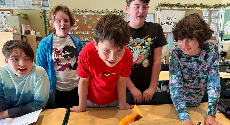 Five teens watching a science experiment in a classroom