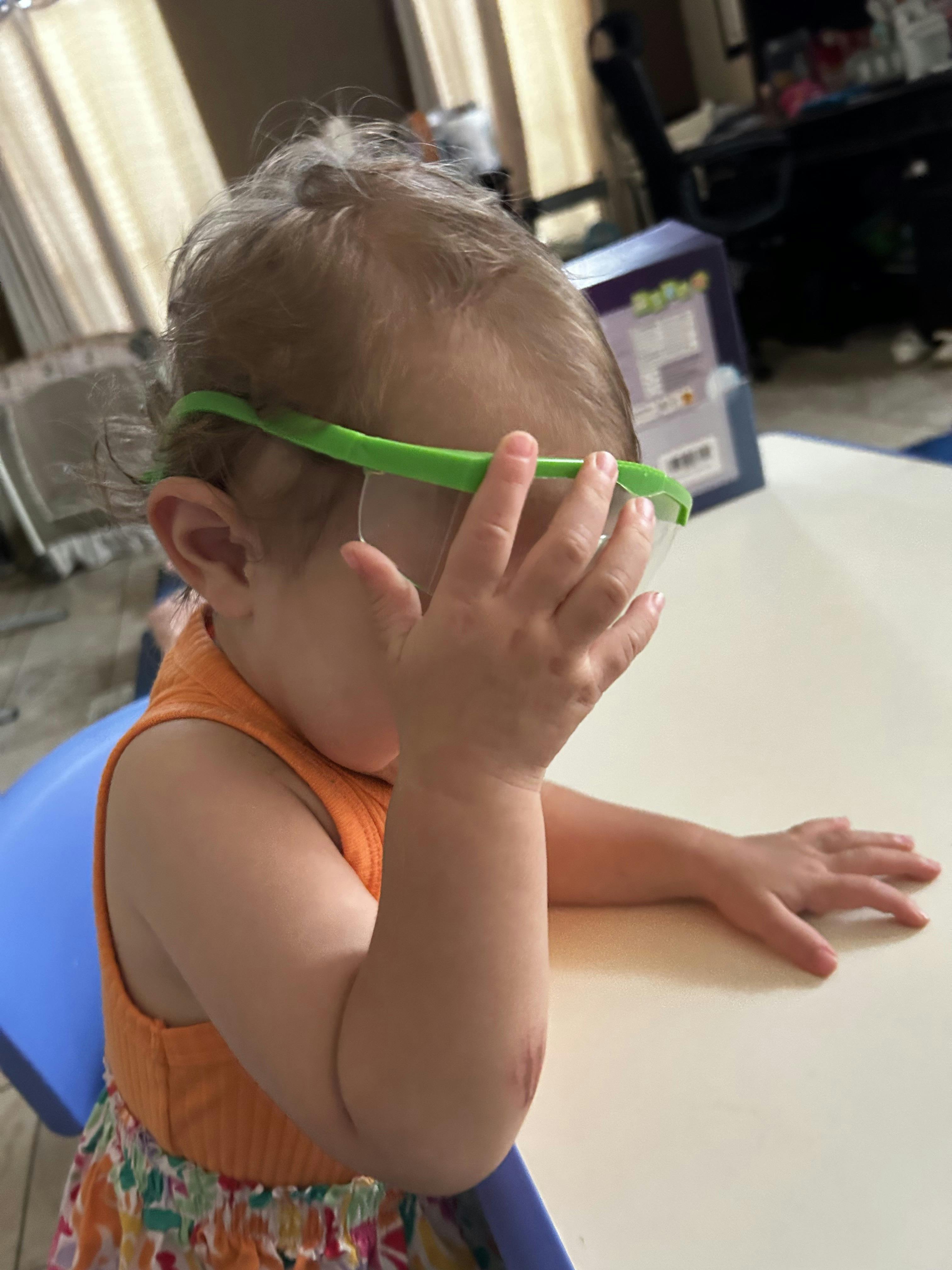 Child wearing safety glasses and covering their face with a hand