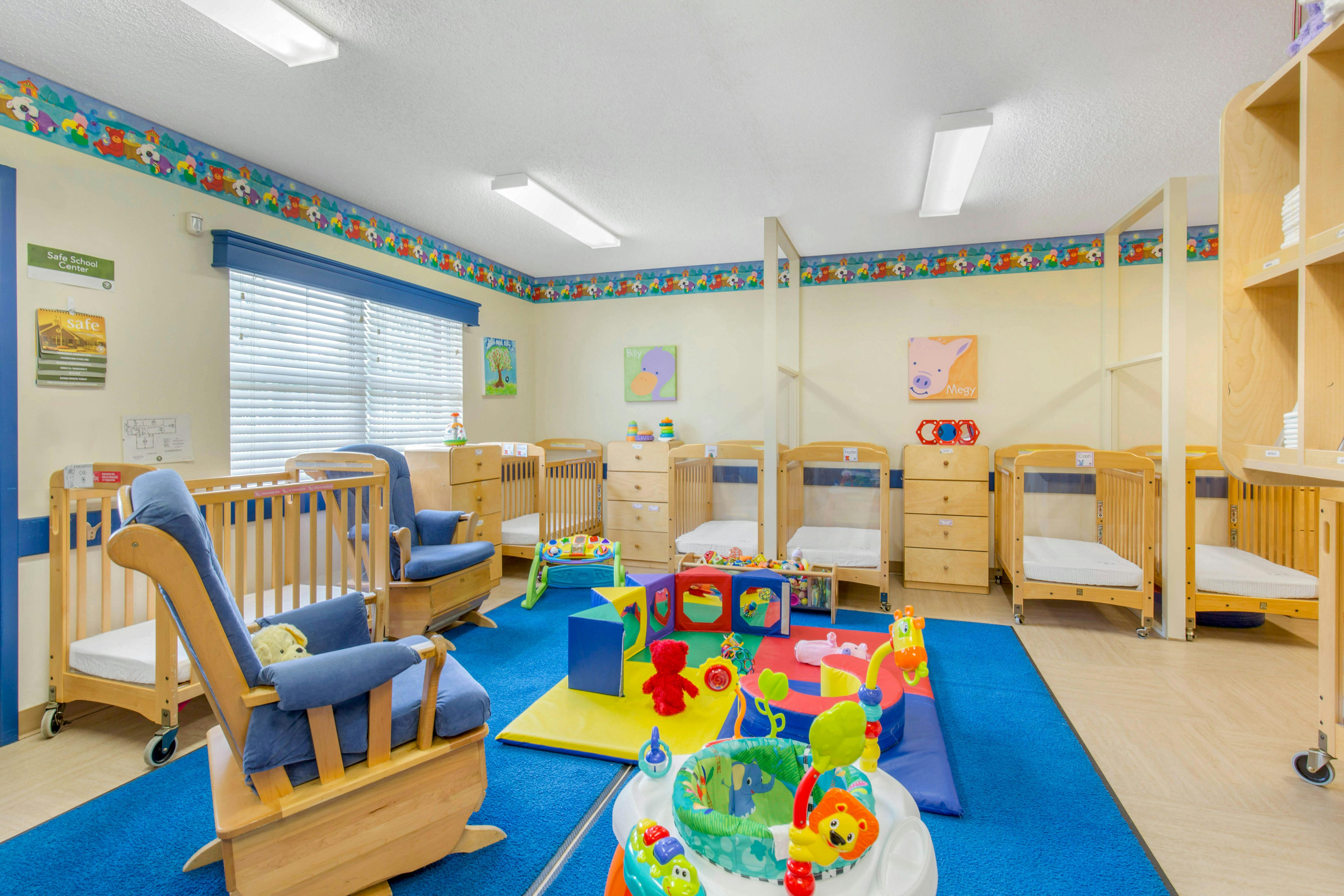 A colorful childcare room with cribs, changing tables, and a blue rug with toys