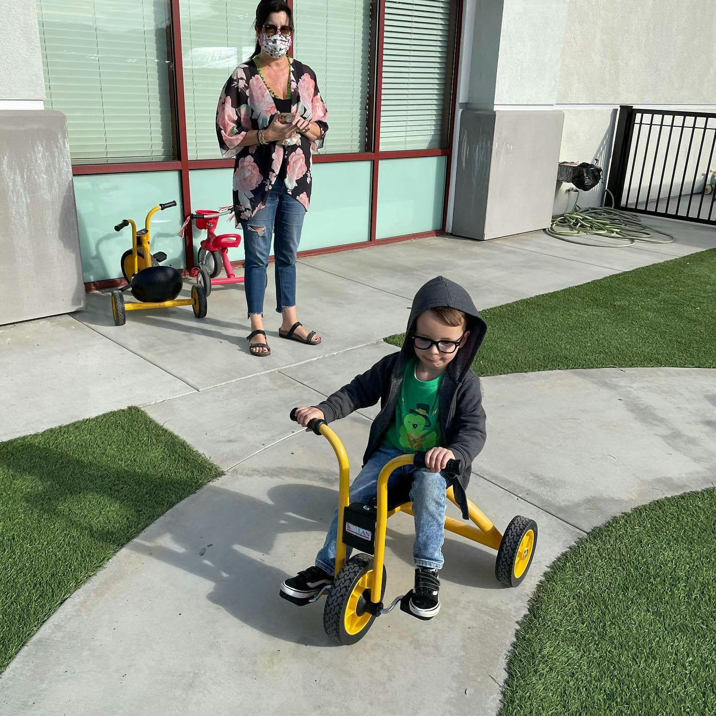 Child on a yellow tricycle with a person standing behind