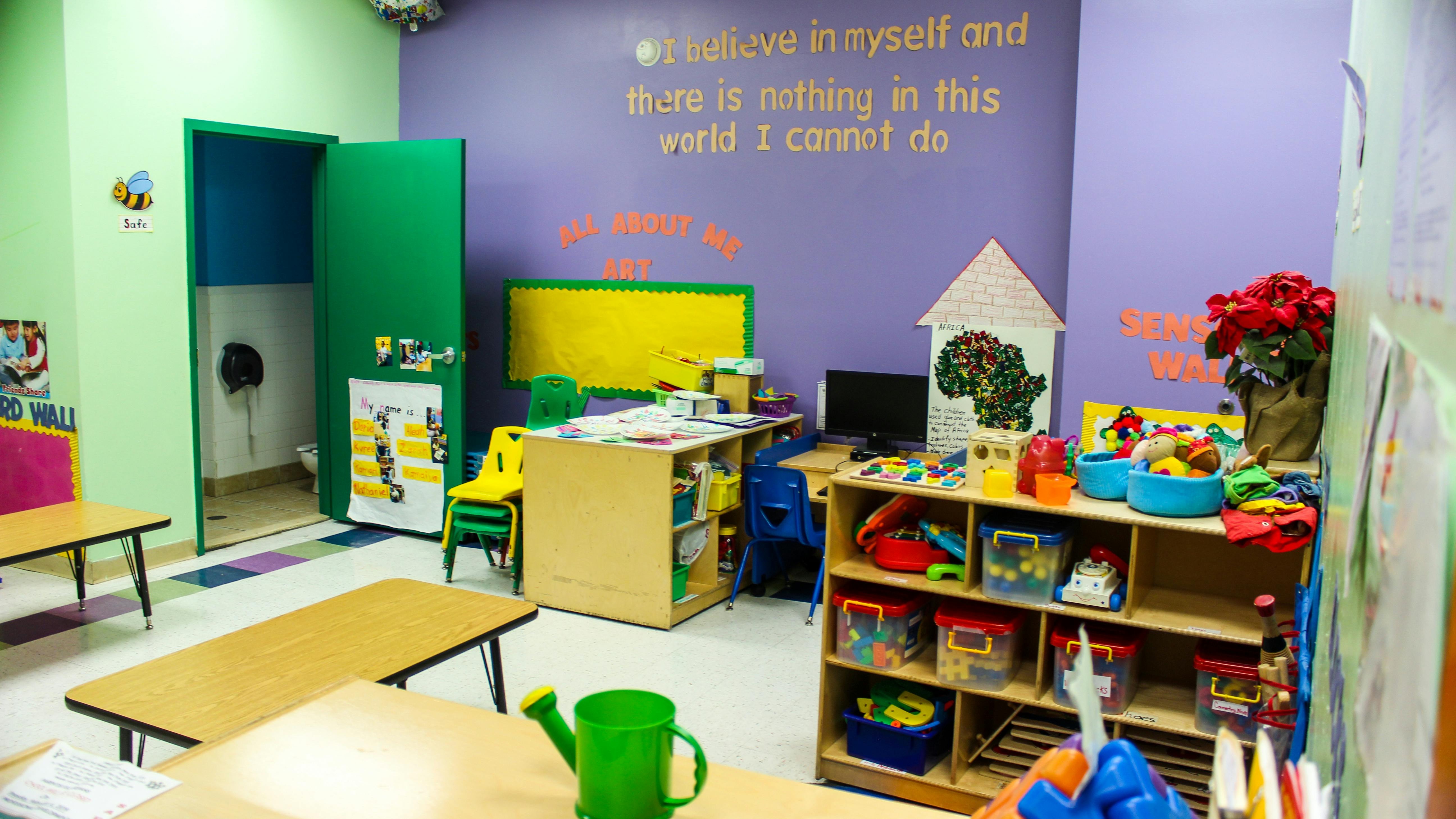 Classroom with small tables, chairs, and shelves with toys
