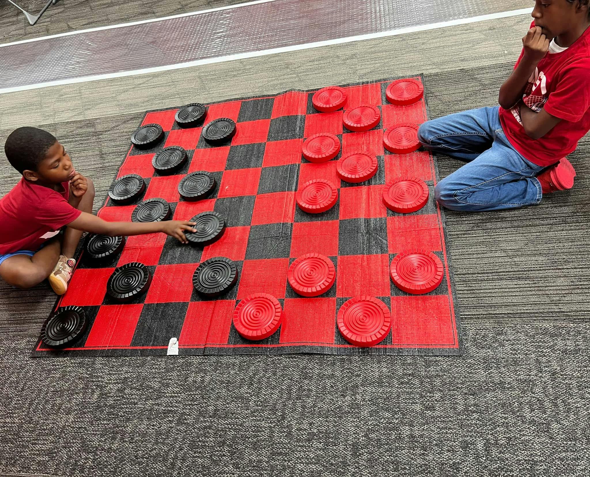 Two children playing checkers on a large red and black board