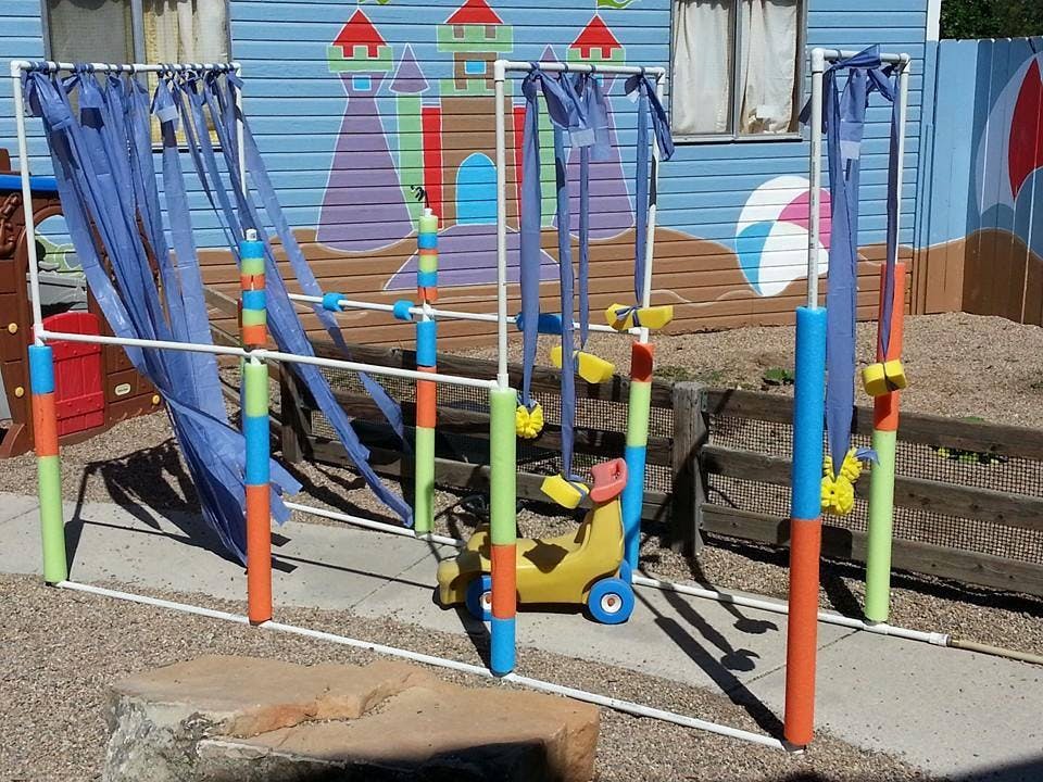 Outdoor play structure with blue fabric strips and a small yellow ride-on toy