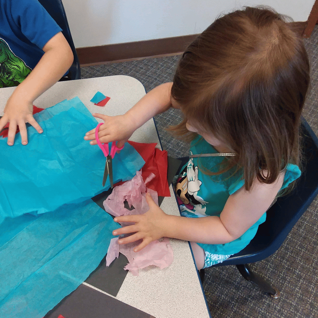 Child cutting blue and pink paper with scissors at a table