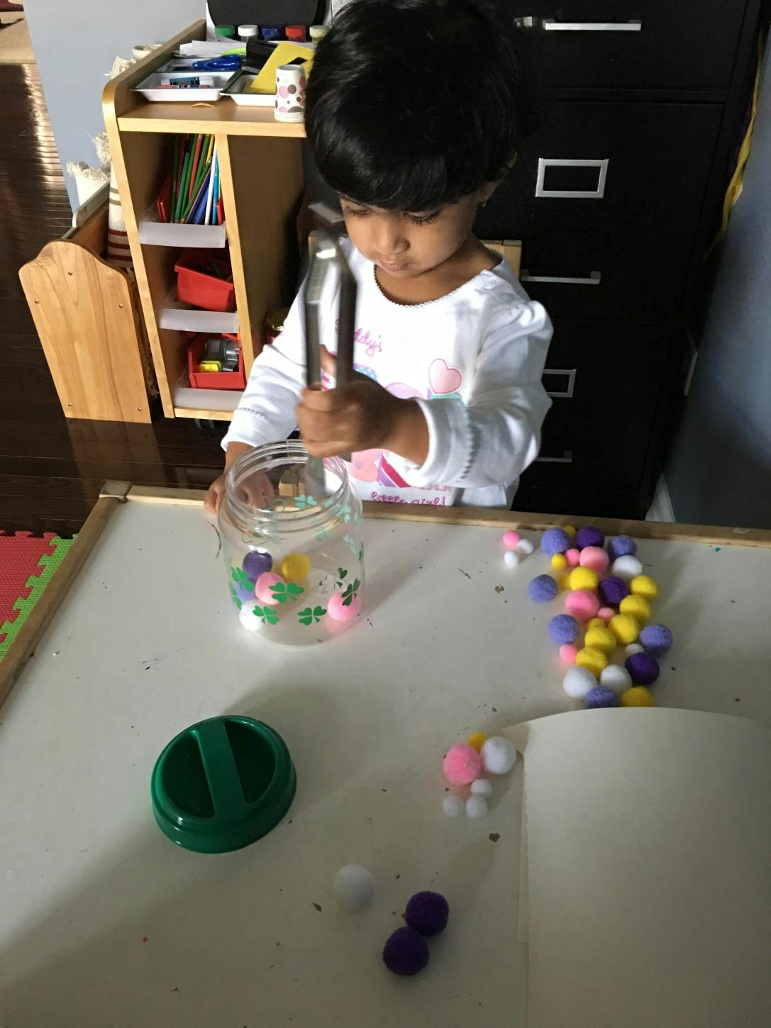 Child using tongs to put pom-poms into a jar