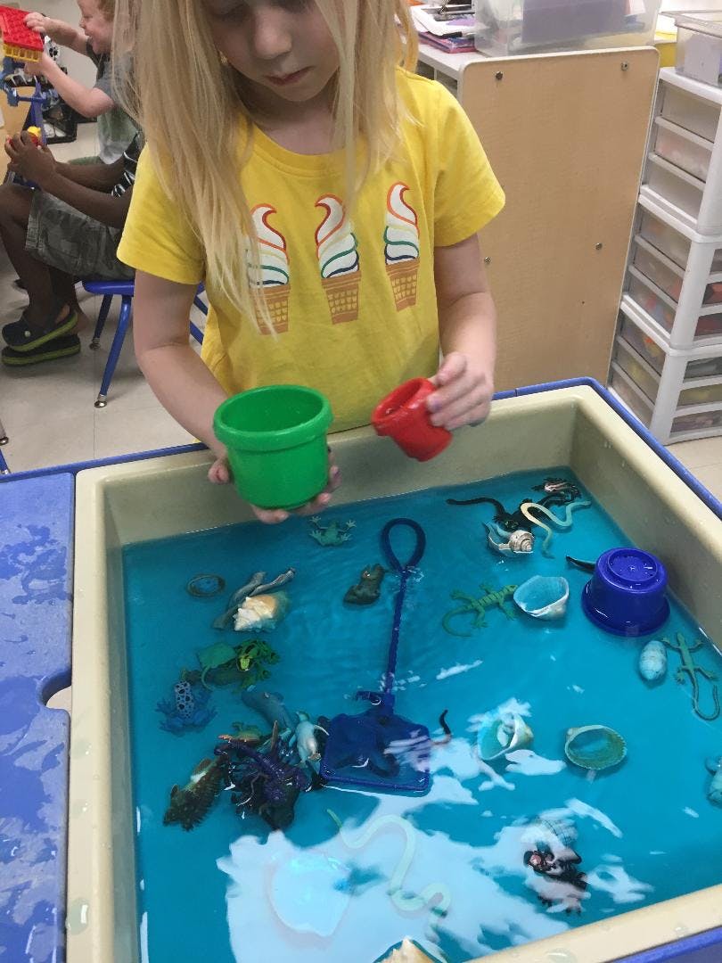 Child playing with cups in a water table