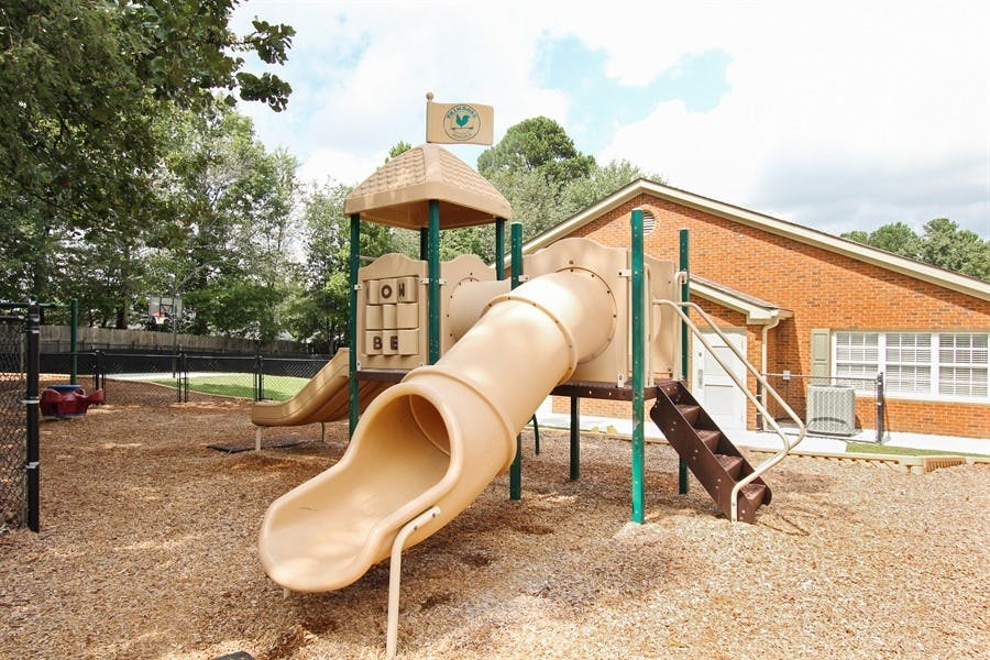 Playground with a tan slide and climbing structure next to a brick building