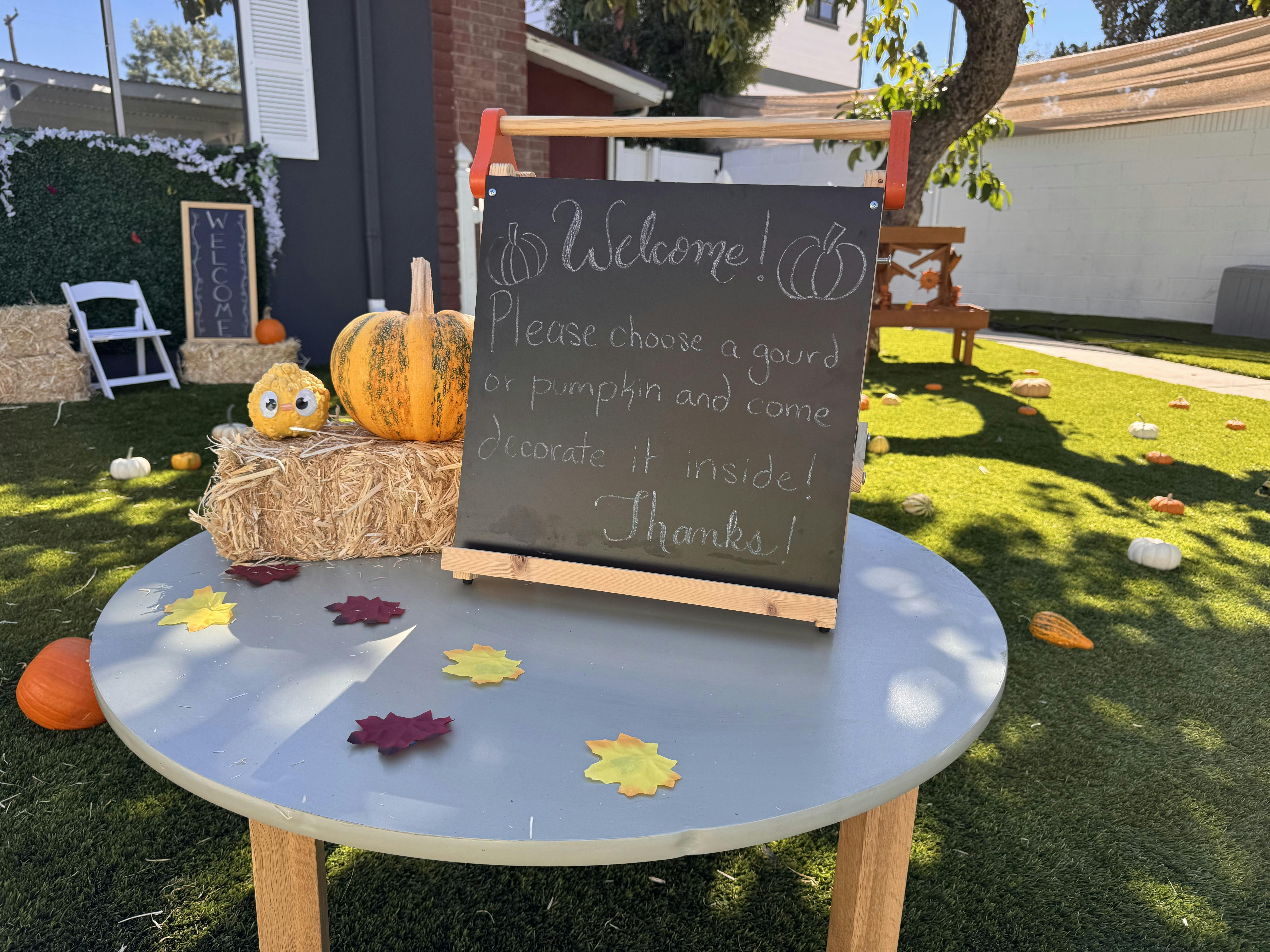 Chalkboard sign on a table inviting people to decorate pumpkins and gourds