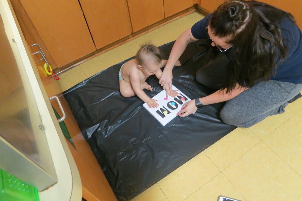 Person and child on floor looking at a sign that says "MOM"