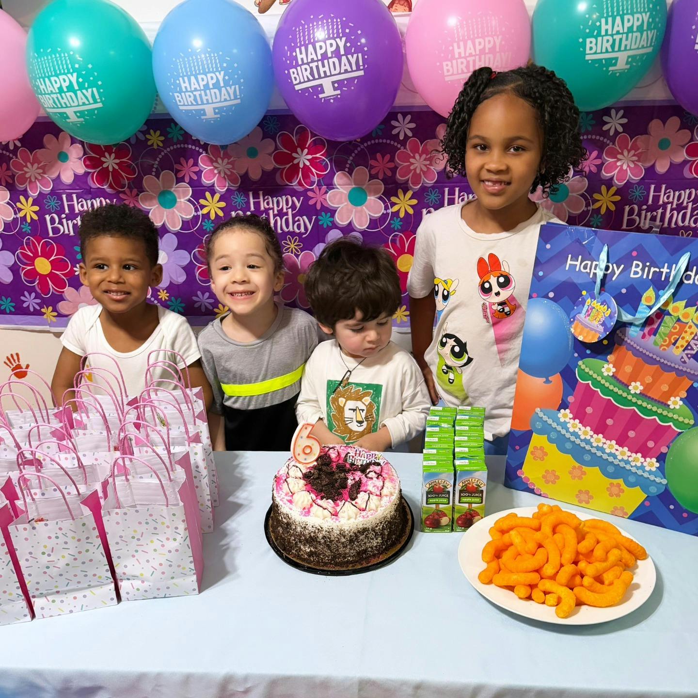 Four children standing behind a table with a birthday cake and party favors