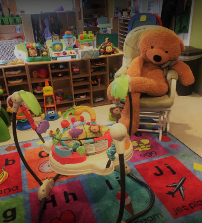 Teddy bear sitting in a chair next to a baby activity center on an alphabet rug