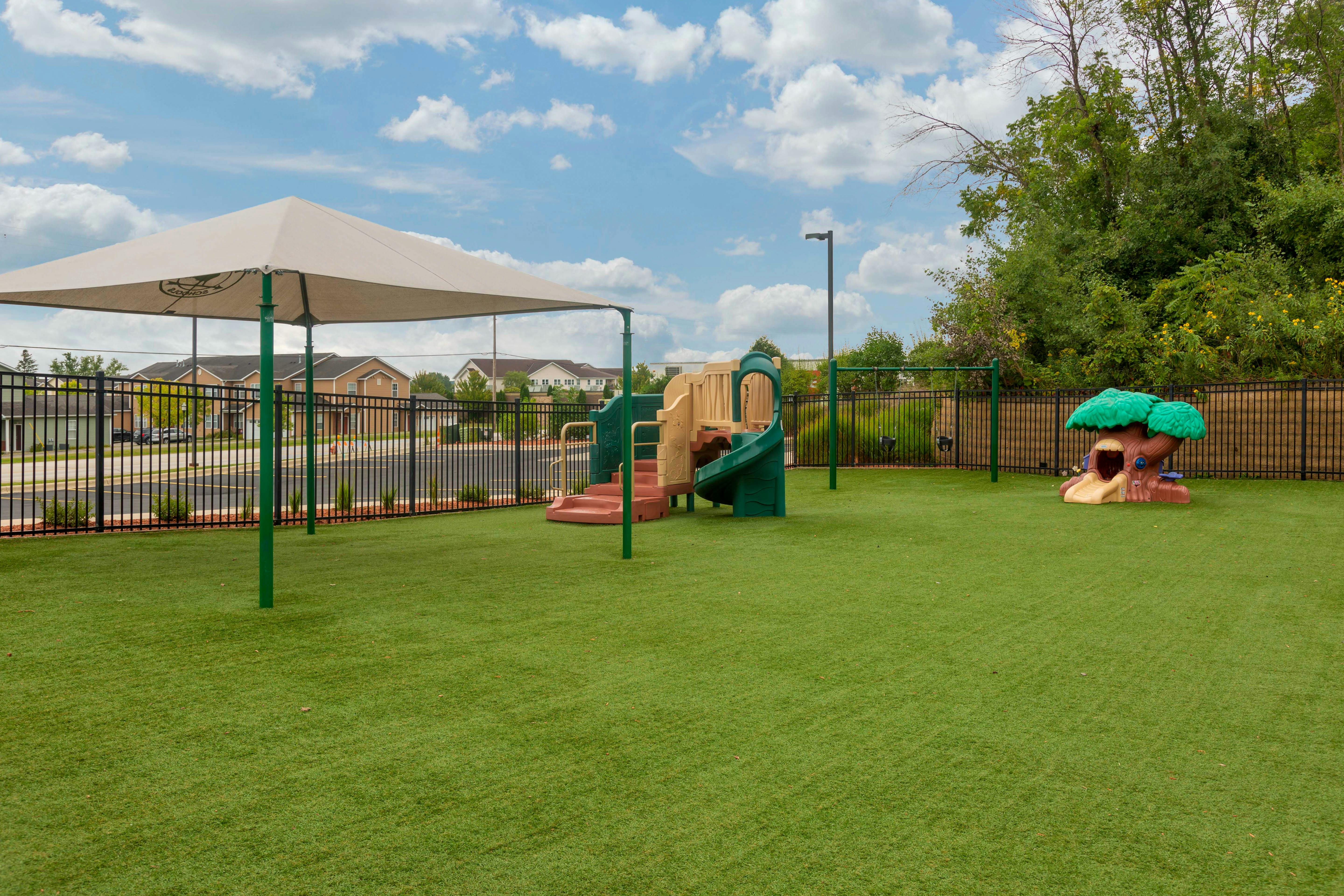 Playground with green turf, a climbing structure with a slide, swings, and a small tree-shaped playhouse